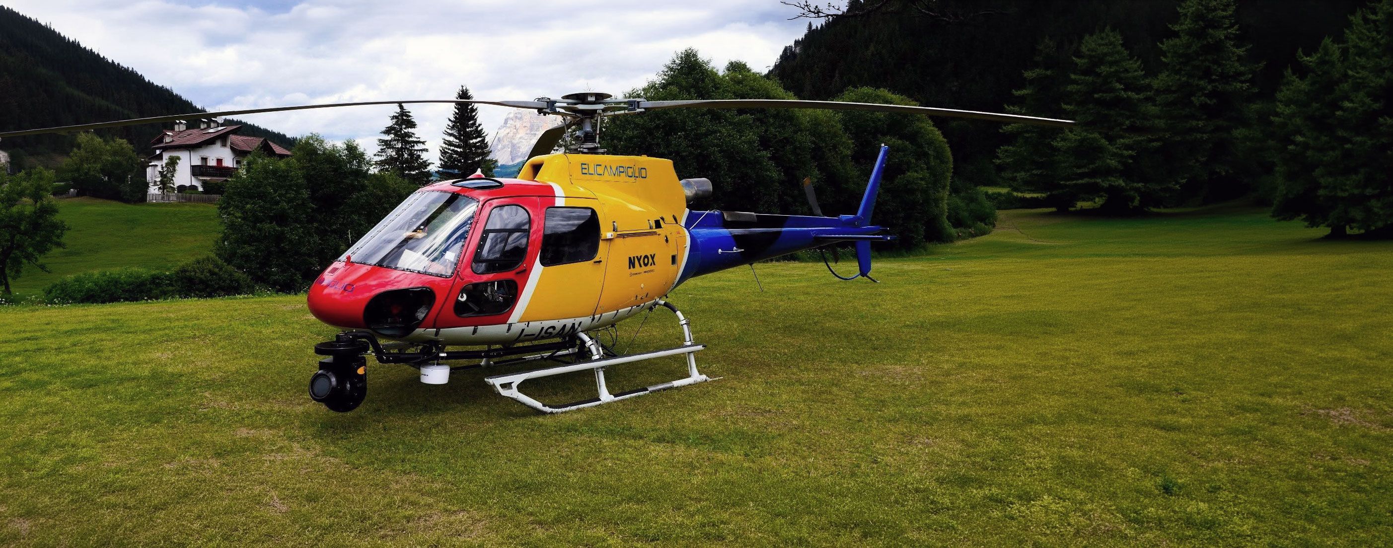 Elicottero AS350 Écureuil su un prato di montagna, con il sistema di ripresa stabilizzato Cineflex montato sul supporto anteriore.